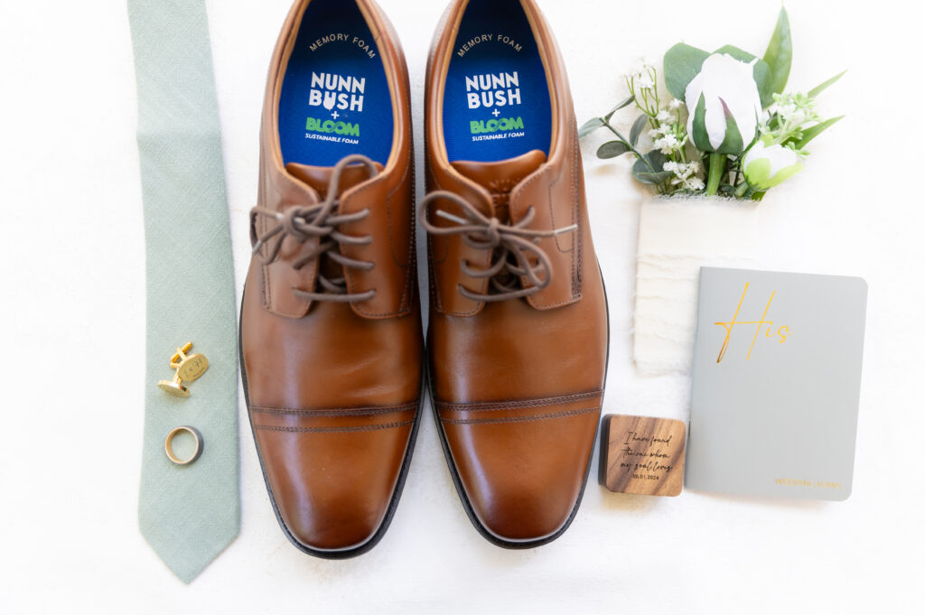 Detail wedding photo of the groom's Colorado wedding day shoes laying next to his tie, ring, boutonniere, ring box, and his vow book