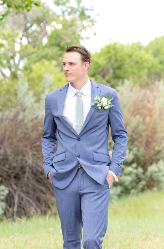 Groom standing with his hands in his pockets looking out in the distance while standing in a grassy field 