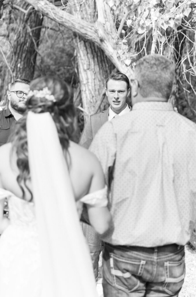 Black and white photo of the groom's reaction to seeing his bride walking down the aisle towards him