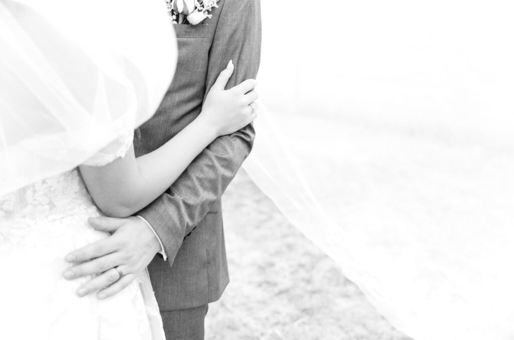 Detail black and white photo of groom pulling his bride in close while putting his hand on her hip and the bride putting her hand on the groom's arm