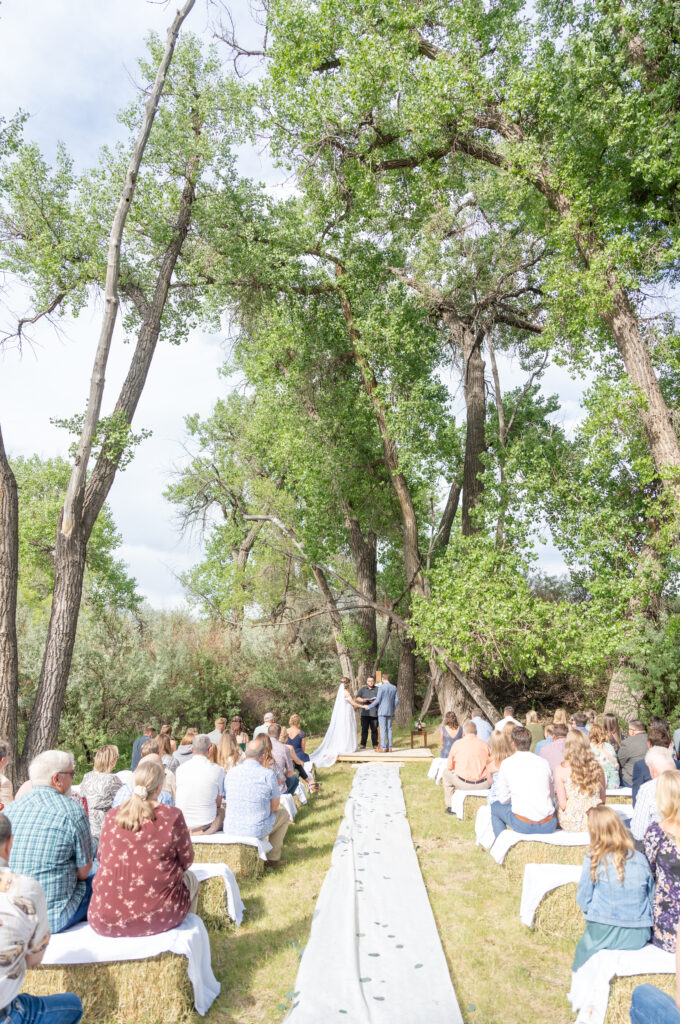 Wide landscape photo of the bride and groom's ceremony location with white runner and tree landscape