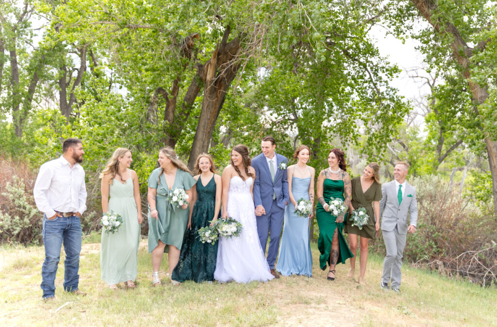 Bride and Groom standing in a grassy field with their wedding party all smiling together and laughing 