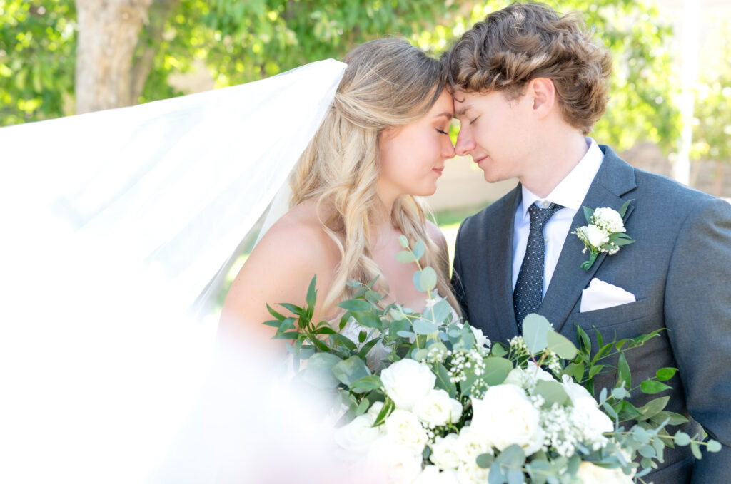 Photo of the bride and groom resting their heads together with a dramatic sweep of the bride's veil in the photo 