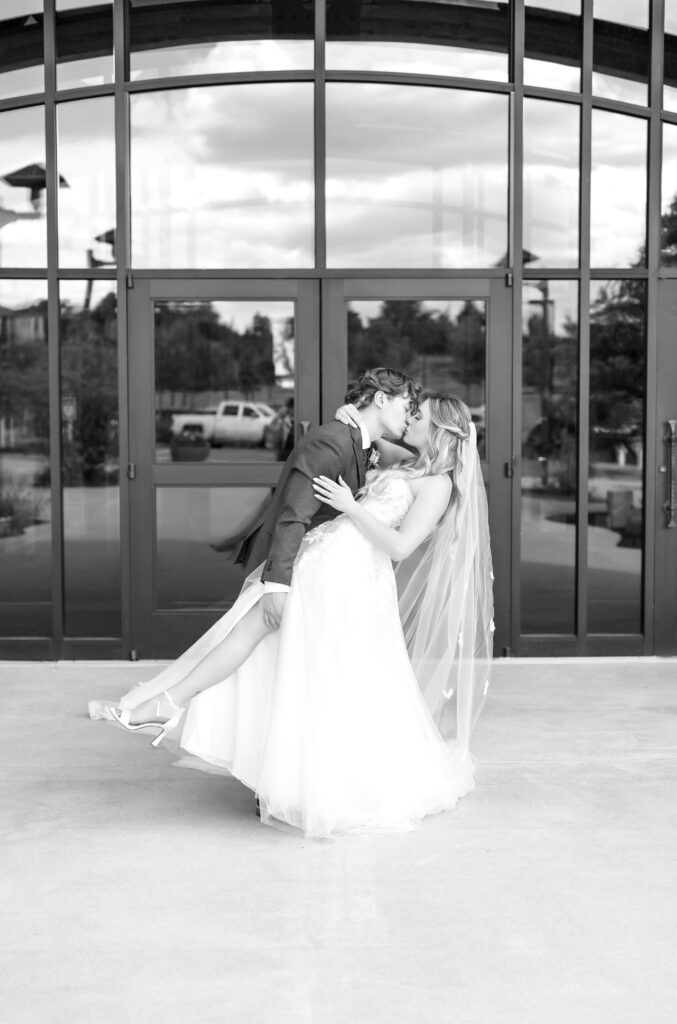 Black and white portrait photo of the groom dipping his bride back for a romantic kiss while holding her leg