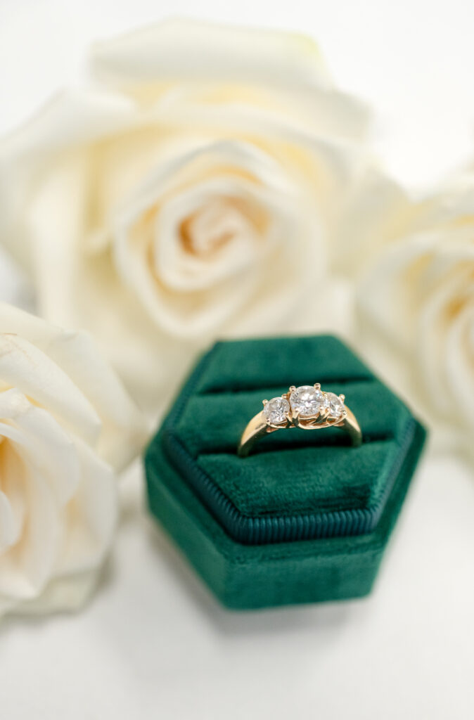 detail photo of bridal ring in a green velvet ring box with white florals sitting behind