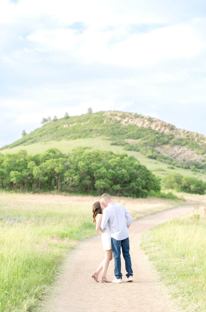 Couple sharing a kiss along trail at Roxborough State Park with mountain view in the background