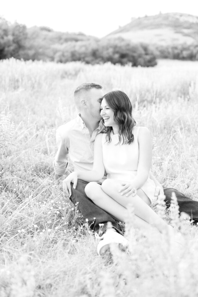 Couple sitting together in field while she is leaning into him and laughing 