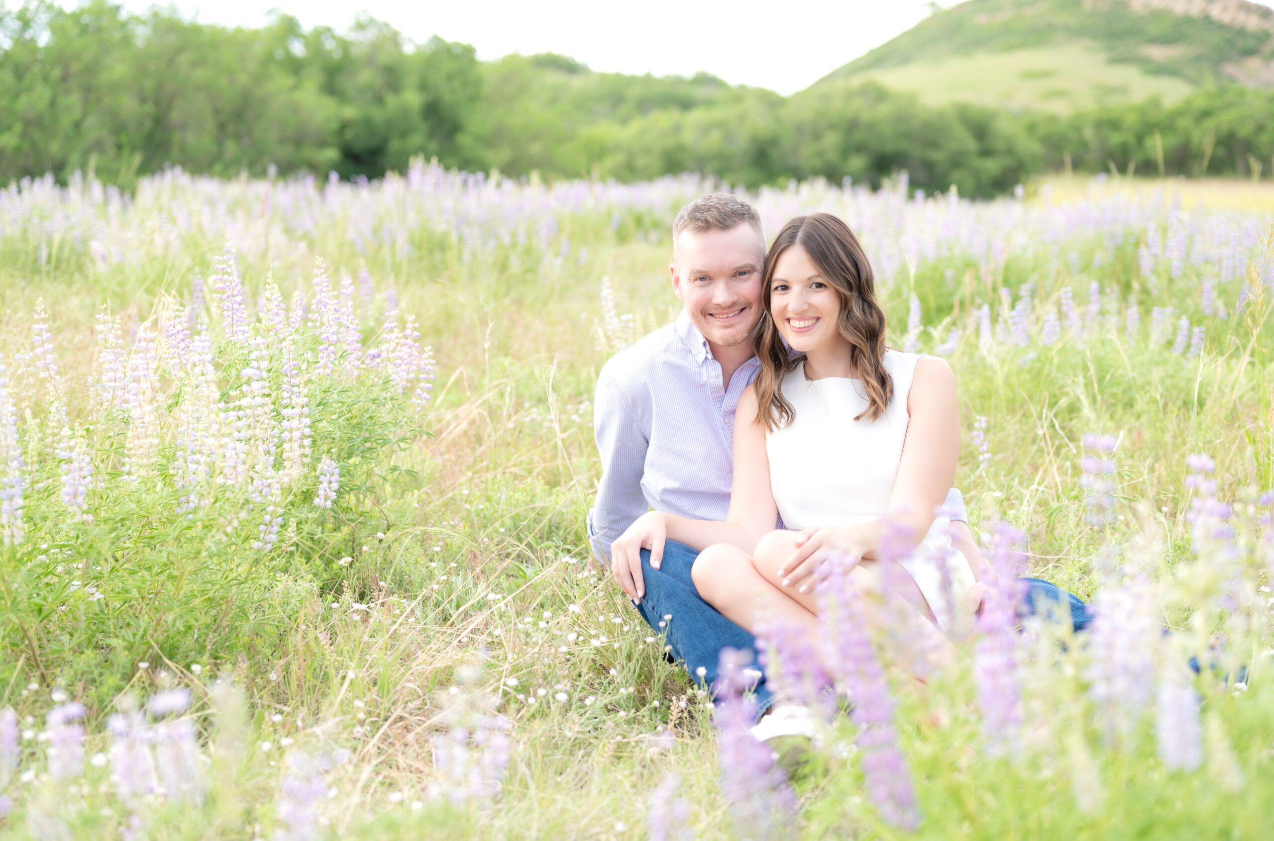 Couple sitting down in grassy meadow field with purple wildflowers at Roxborough State Park in Colorado