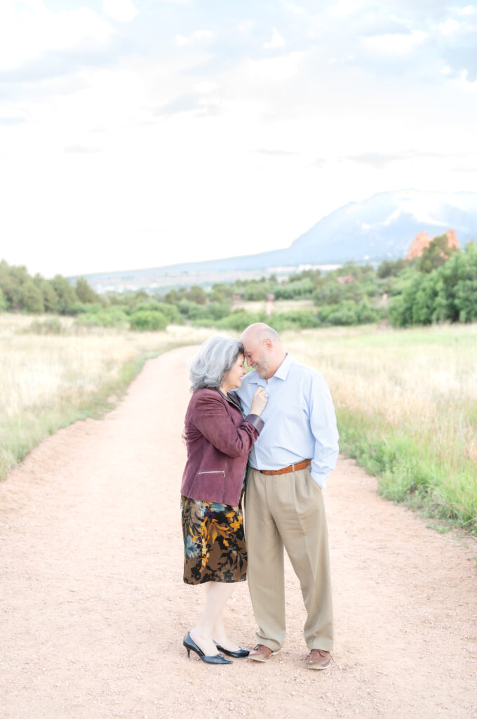 Style guide for classic and timeless family photos, older couple stand on a gravel path with mountains in the background leaning into each other and touching foreheads