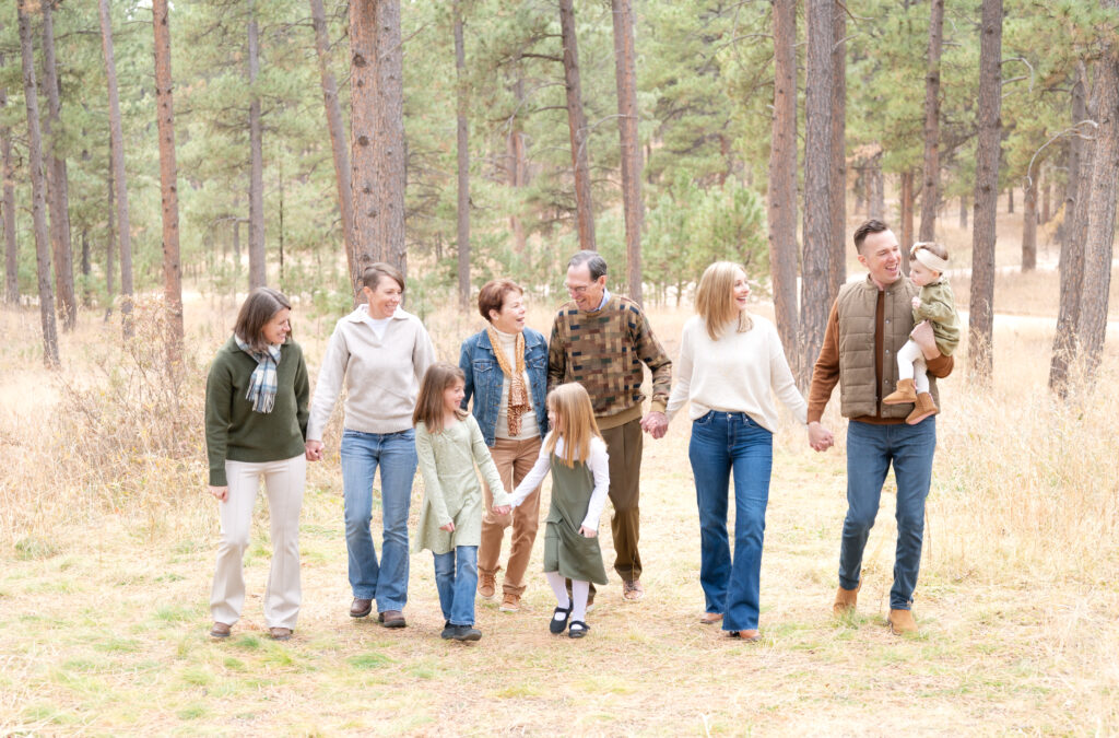 Extended family walking through the woods in Colorado wearing muted fall colors like brown, cream, sage, and blue.