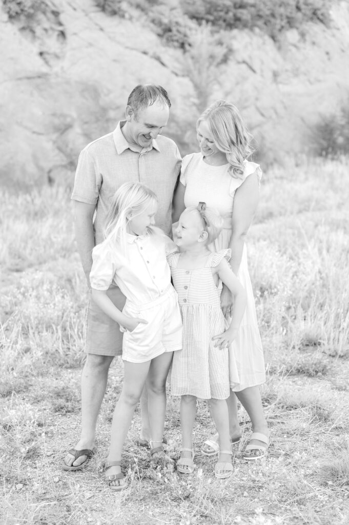 Black and white photo of two sisters with their arms around each other and their parents smiling down at them from behind