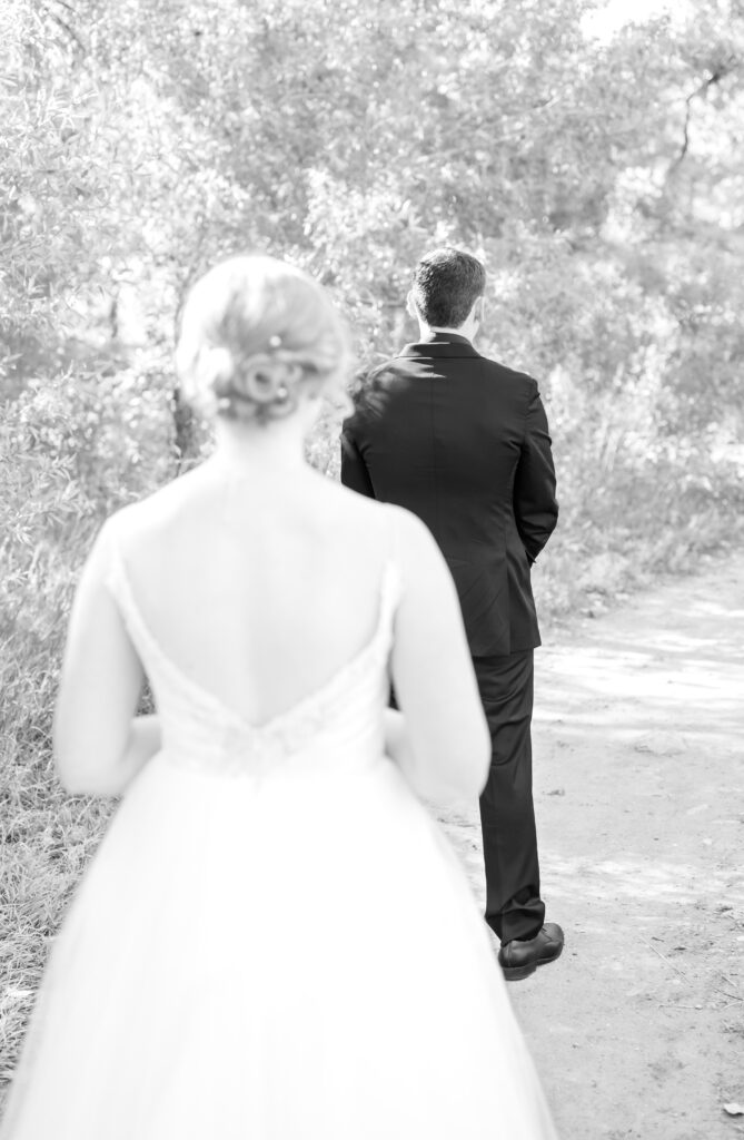 Bride walking up behind her groom on path to share first look moment with her groom on their wedding day in Colorado Springs