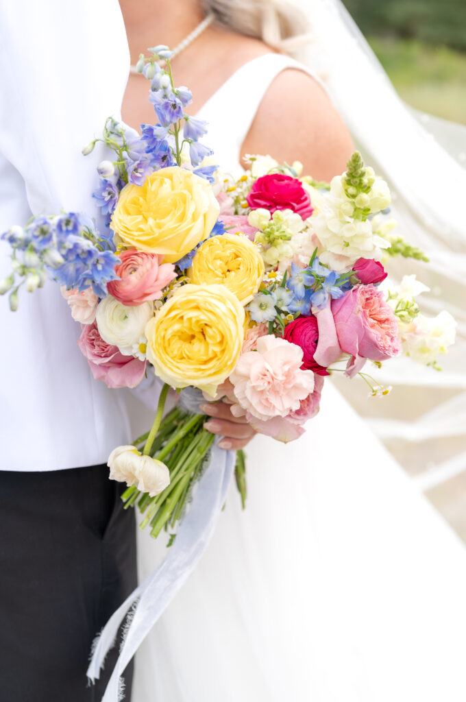 Bright bouquet of pink and yellow roses being held by bride as she kisses the groom