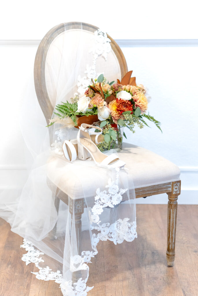 Chair draped with bridal veil and holding bride's shoes and beautiful bouquet