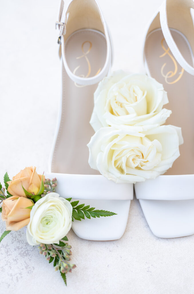 Detail of white bridal shoes with roses arranged around them