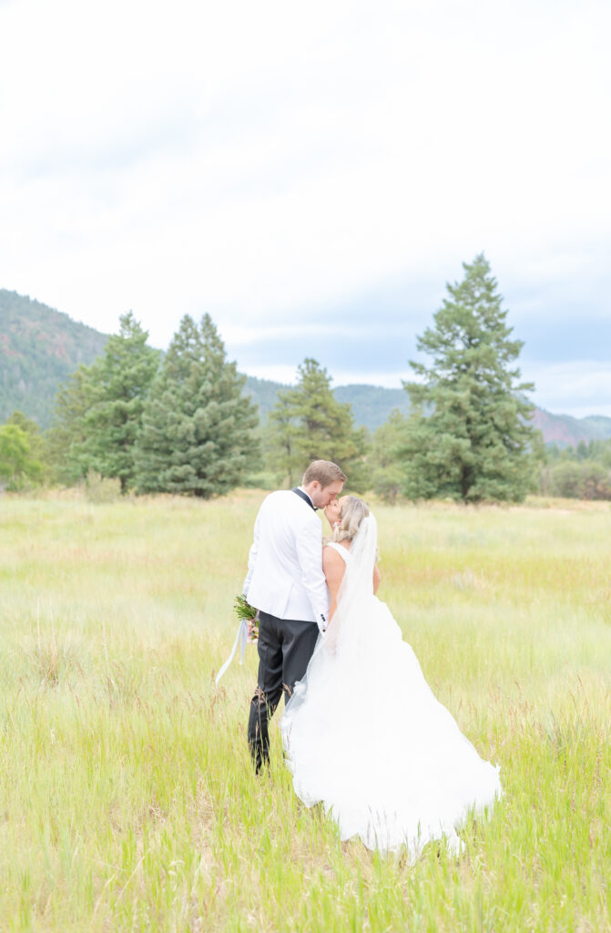 Bride and groom exchange a kiss in a field hemmed by mountains in Colorado