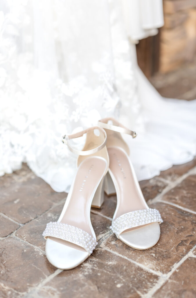 Jeweled bridal shoes set on cobblestones with the hem of the bride's dress draped behind them