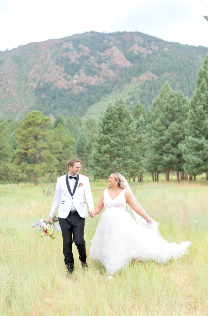 Bride and groom holding hands and smiling at each other as they stroll together through the Colorado landscape