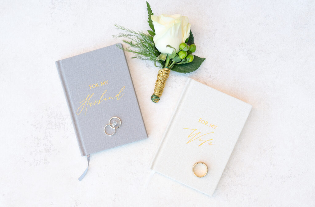 Wedding detail photo of bride and groom vow books and the groom's boutonniere