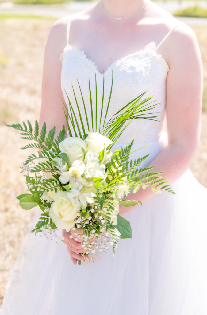 Close detail photo of bride holding her greenery bridal bouquet up against her white dress