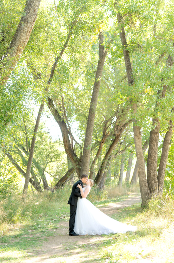 Bride and groom exchange a passionate kiss as they stand together on a wooded path