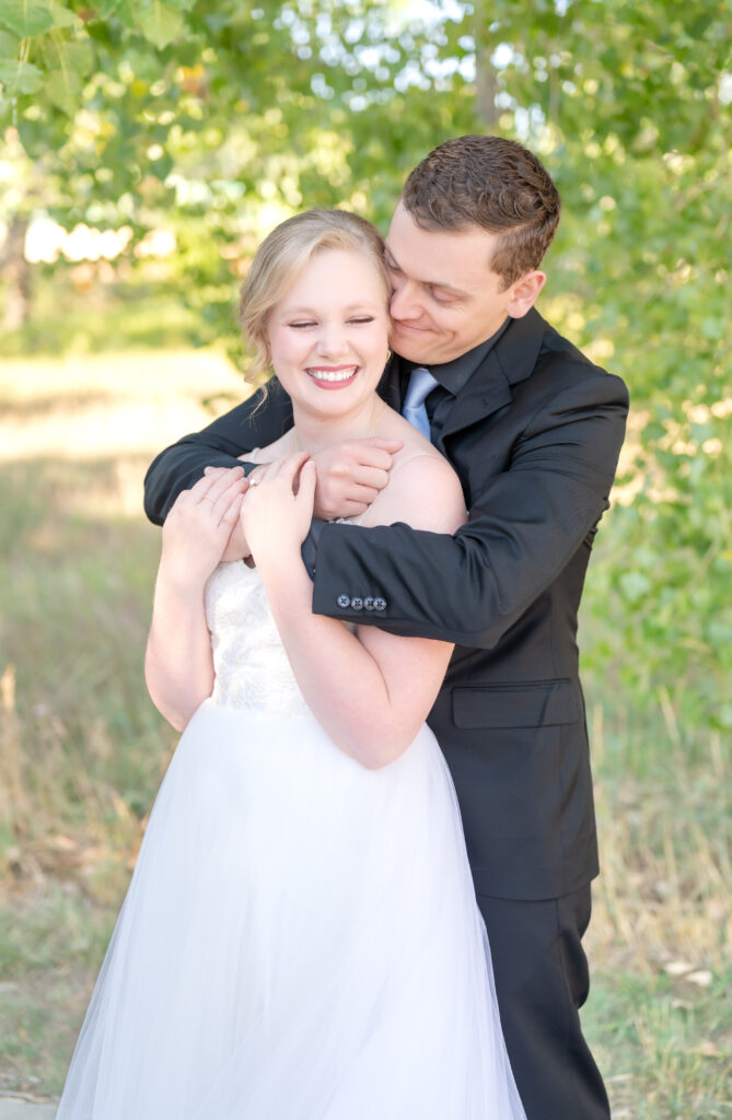 Groom pulling his bride in for a close hug smiling down at her on their wedding day in Colorado springs 