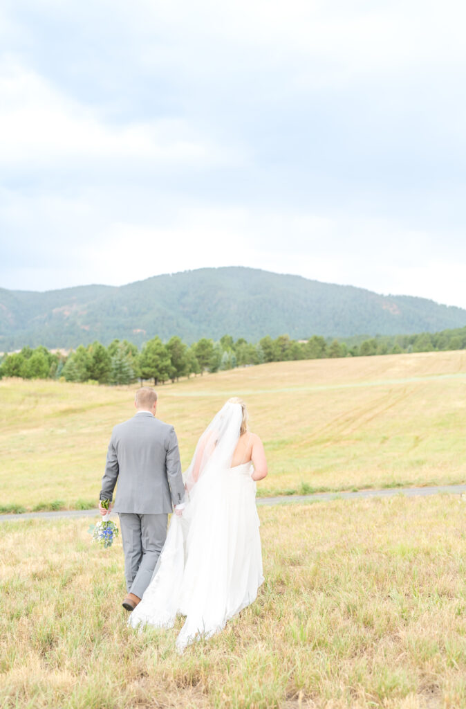 Bride and groom walking hand-in-hand across the fields toward the mountains of Colorado 