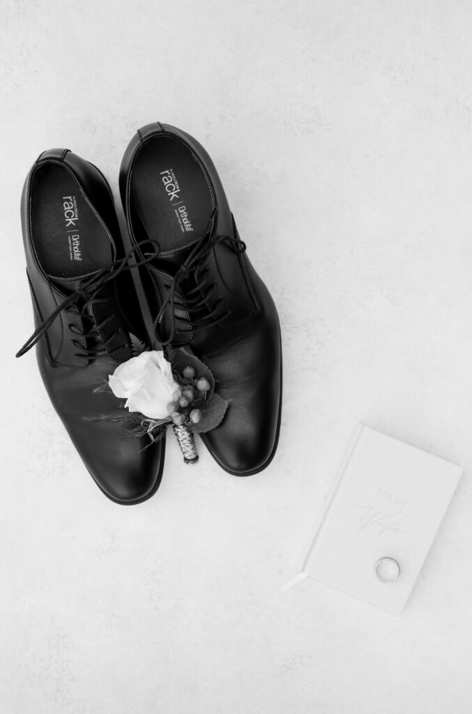 wedding detail photo of the groom's boutonniere laying on his shoes, his vow book, and his ring