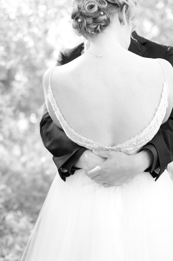 Detail photo of the groom wrapping hiss arms around the bride to pull her in for a tight, embracing hug during their first look moment on their wedding day 