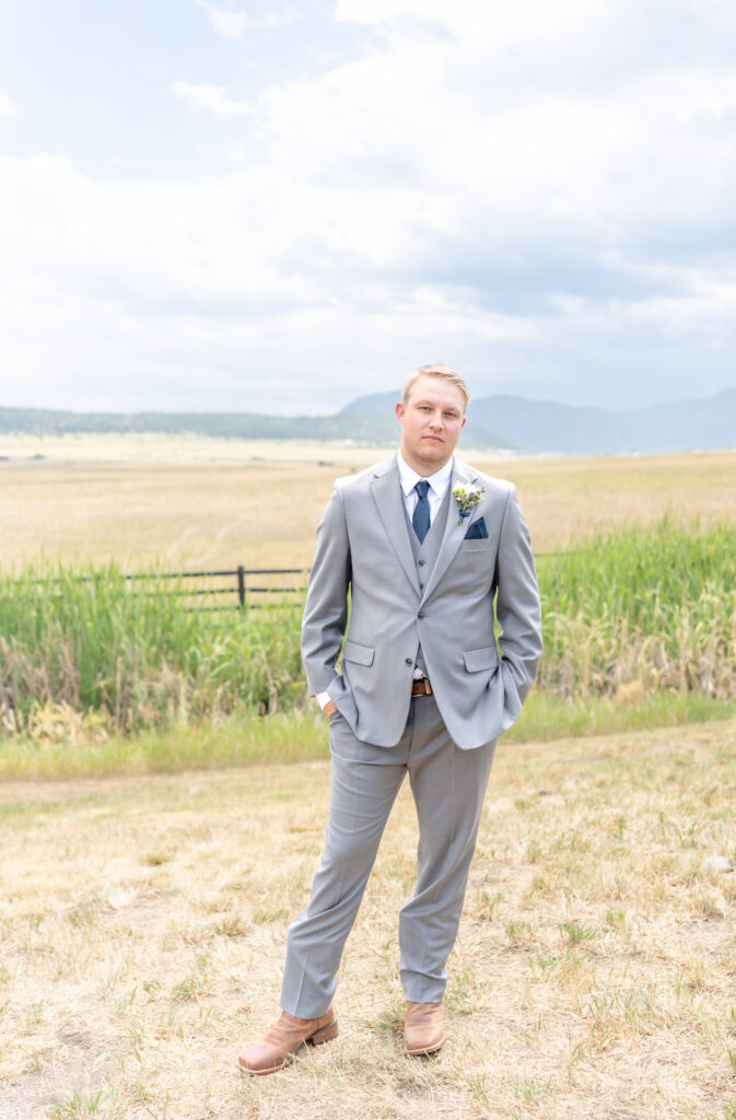 Groom poses in a field with a backdrop of distant mountains behind him