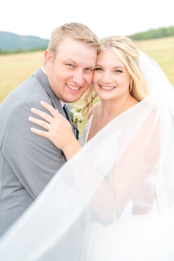 Newly married couple in their wedding outfits embrace, smiling at the camera