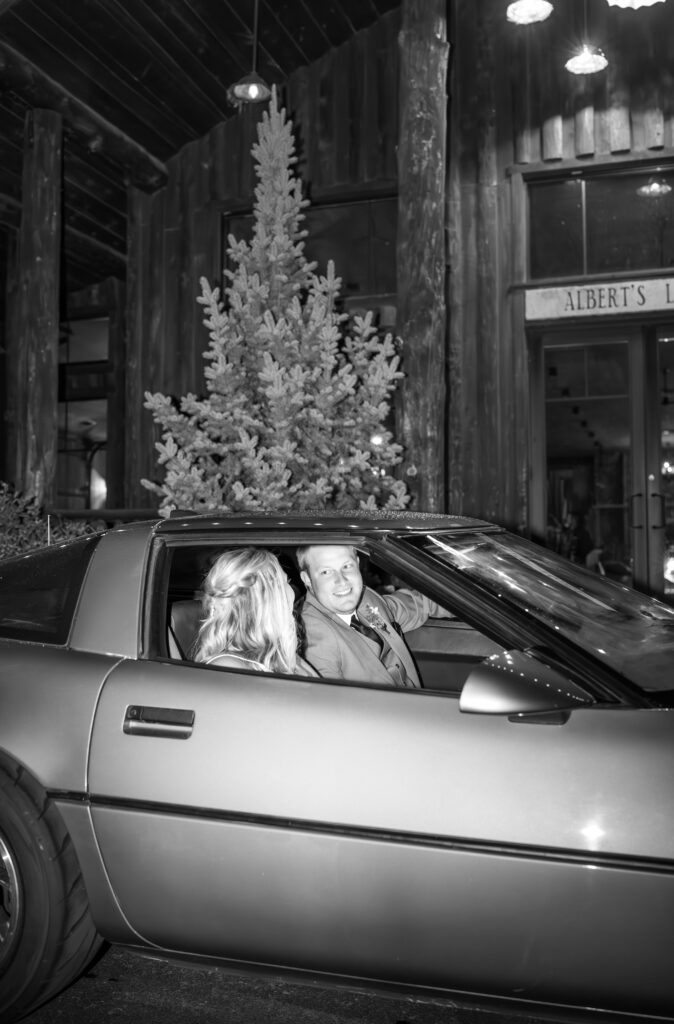 Black and white flash photo of bride and groom sitting in retro car as they get ready to make their exit