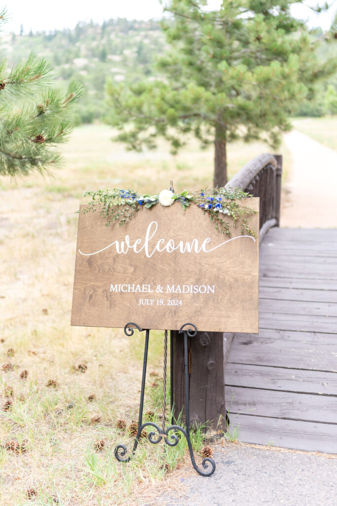 Sign near wooden footbridge welcoming guests to a wedding at Spruce Mountain Ranch in Larkspur, CO