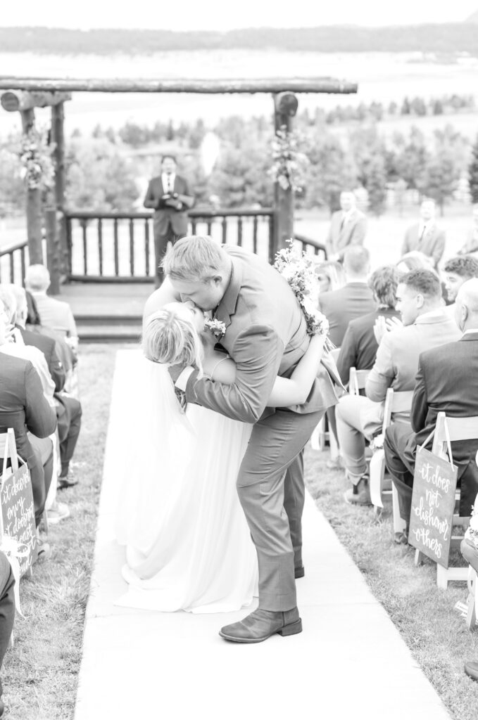 Black and white image of groom dipping his bride as they kiss in the aisle following their wedding ceremony