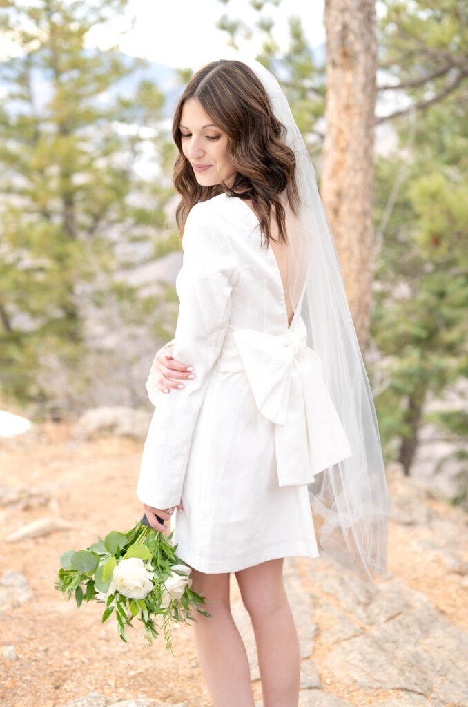 Bride holding her elbow as she looks down over her shoulder with a soft smile and holding her bridal bouquet down in her other hand