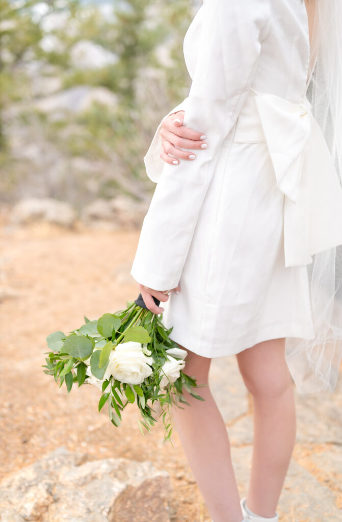 Closeup of the bride holding her white floral and greenery bridal bouquet in one hand and the other hand is placed softly on her elbow