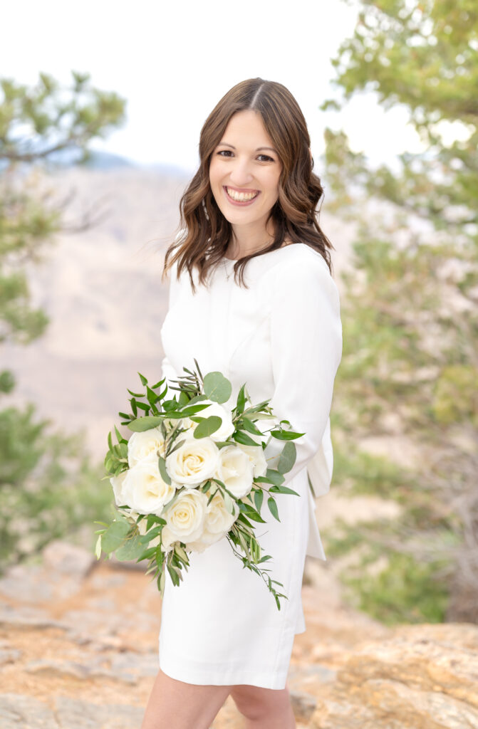 Bride smiling at the camera as she holds her bridal bouquet in her arms 