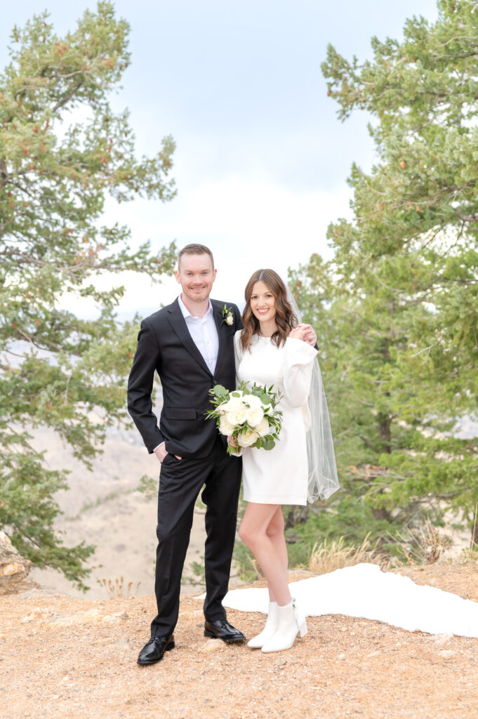 Groom wraps his arm around his bride's shoulder as they hold hands and smile toward the camera for their couples photos at Lookout Mountain