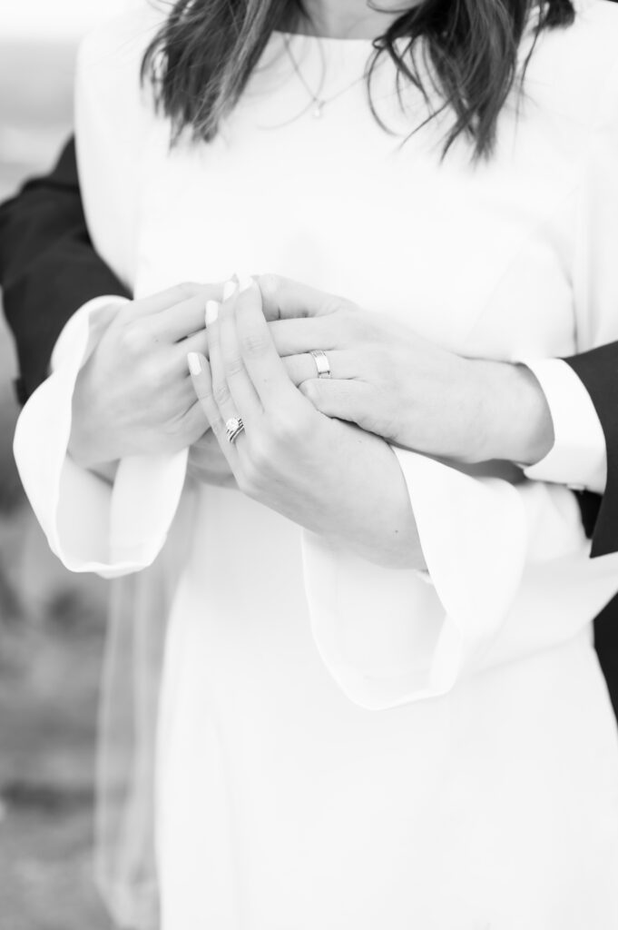 Closeup black and white edited photo of the bride and groom holding hands together and showing close up of their rings