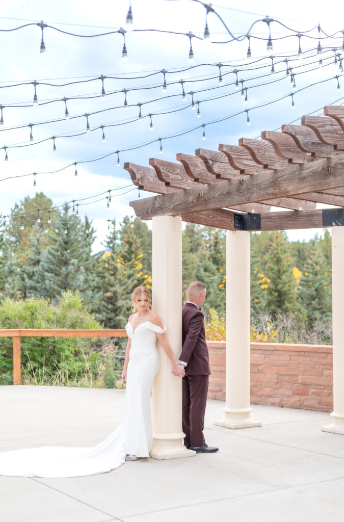 Bride and groom reach around a pillar to hold hands on the patio at Deer Creek Valley Ranch Colorado on their wedding day