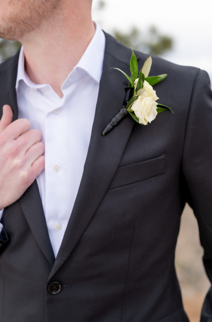 Closeup of the groom's white floral and greenery boutonniere on his black suit jacket