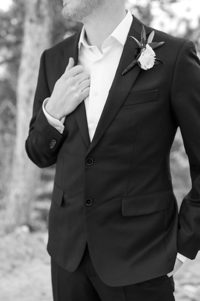 Closeup black and white photo of the groom holding the lapel of his black jacket