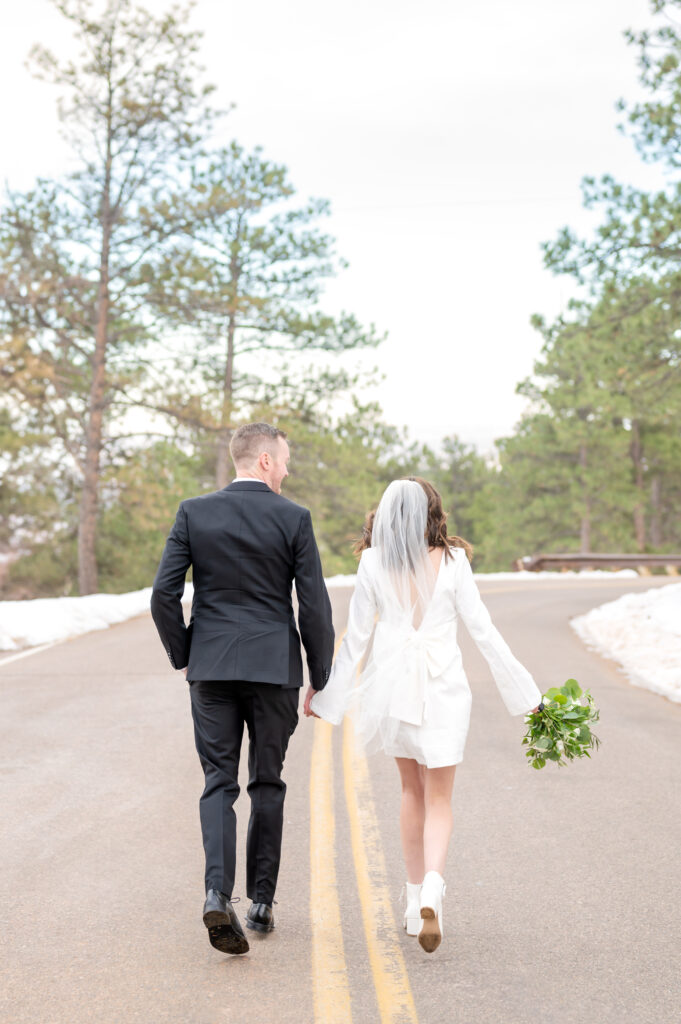 Bride and Groom lightly run and hold hands along the road together to celebrate their elopement at Lookout Mountain in Colorado