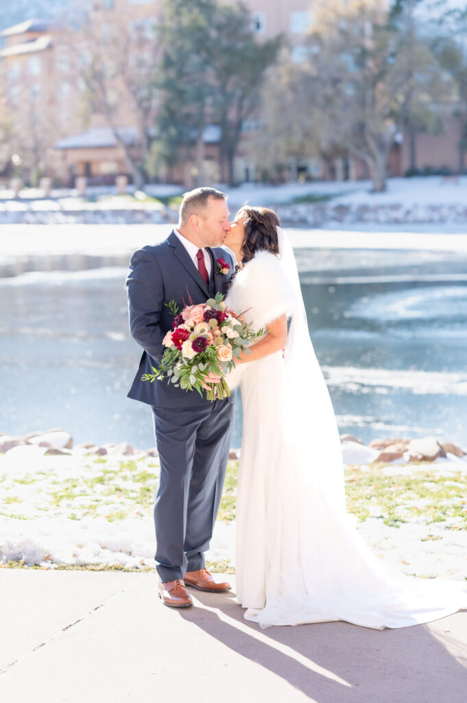 Newly married couple exchange a kiss by the pond at Broadmoor wedding venue in Colorado