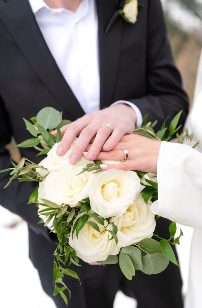 Closeup of the bride and groom laying their hands together on top of the bride's bridal floral bouquet 