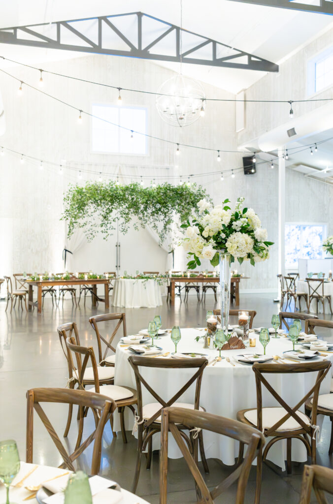 Interior of Woodlands white barn wedding venue in Colorado, strung with lights and decorated with white and green florals