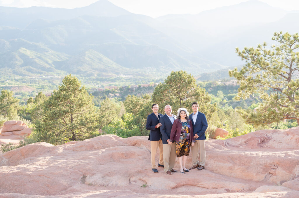Couple with their grown sons standing on a red rock outcrop in Garden of the Gods with beautiful mountain background