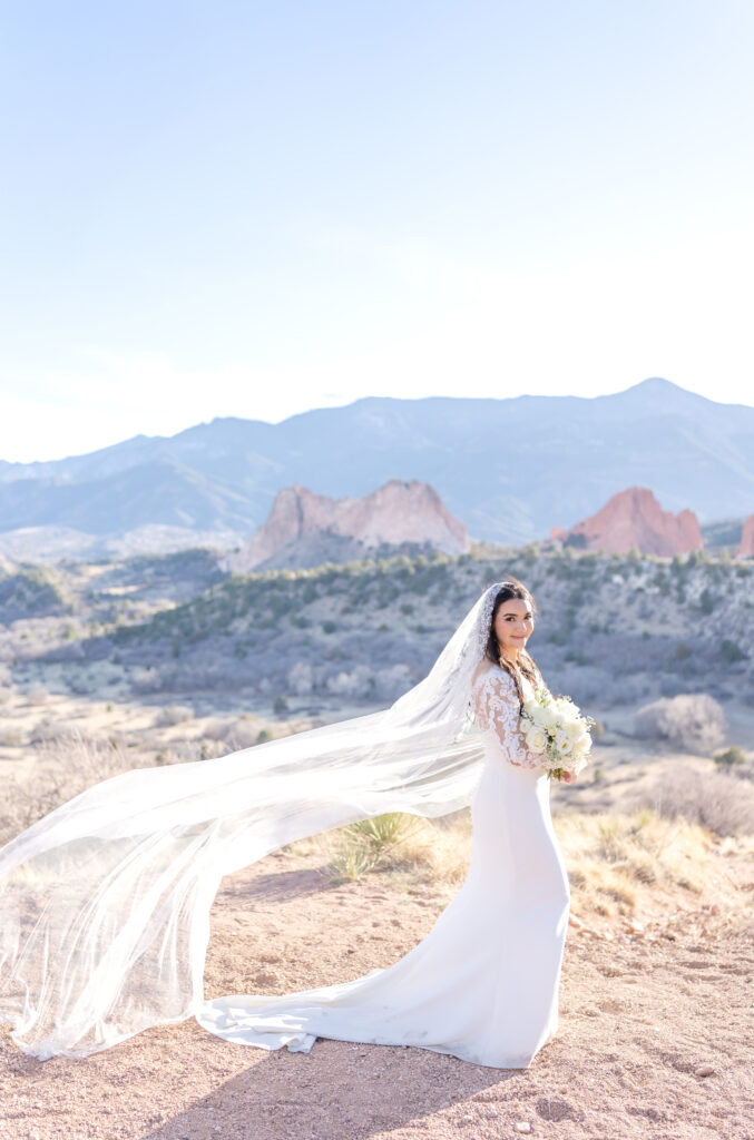 Bride smiling while holding her flowers and her veil flowing in the wind behind her