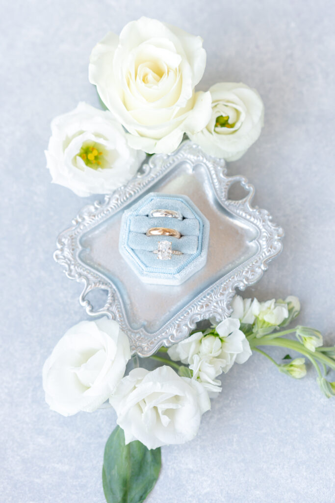 Wedding detail photo of blue velvet ring box on silver dish tray with white florals and greenery around