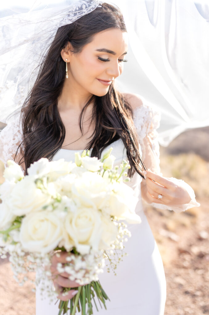 Bride holding her white floral flower bouquet while also holding her hair in one hand and smiling looking down over her shoulder